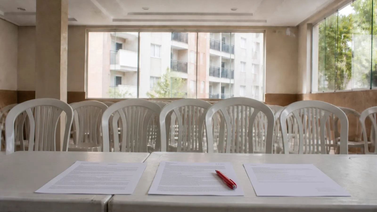 Documentos impressos e caneta vermelha sobre a mesa de uma sala de assembleia vazia