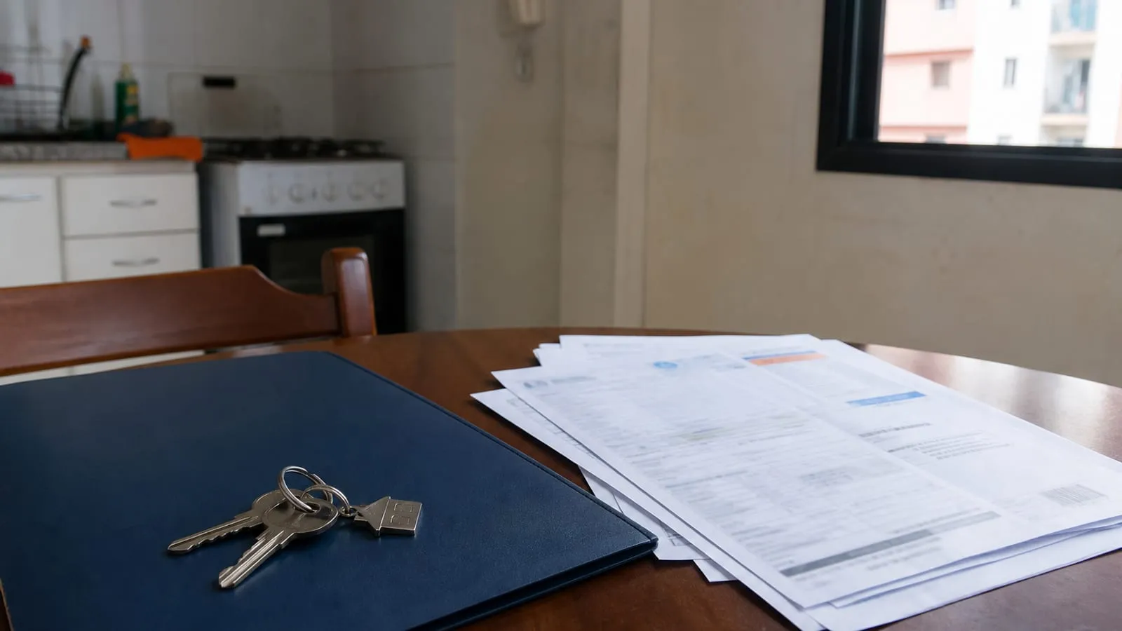 Chaves de apartamento sobre uma pasta de contrato e contas em uma mesa de cozinha